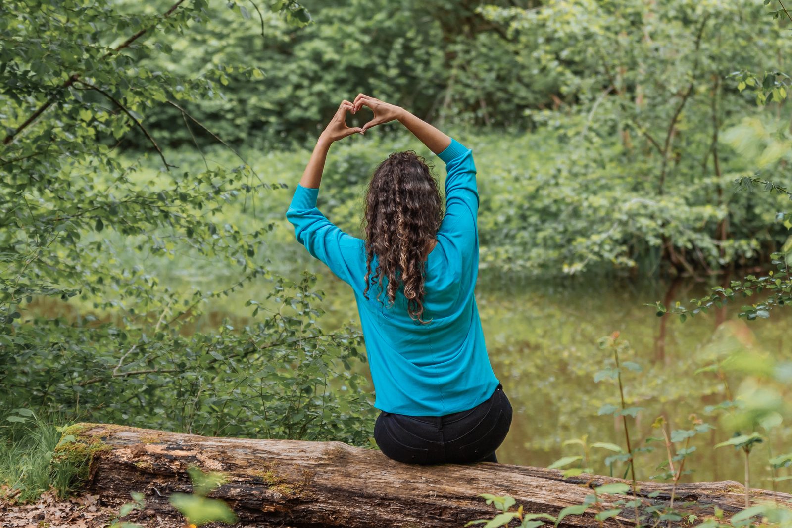 Sarah formt mit den Händen ein Herz über dem Kopf, am Waldsee